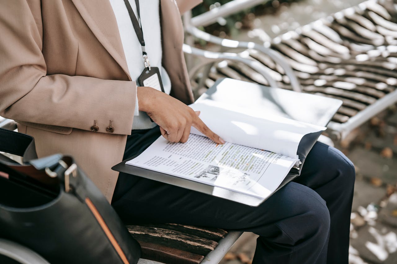 A woman reviewing documents on a park bench during daytime, focusing on work or study.